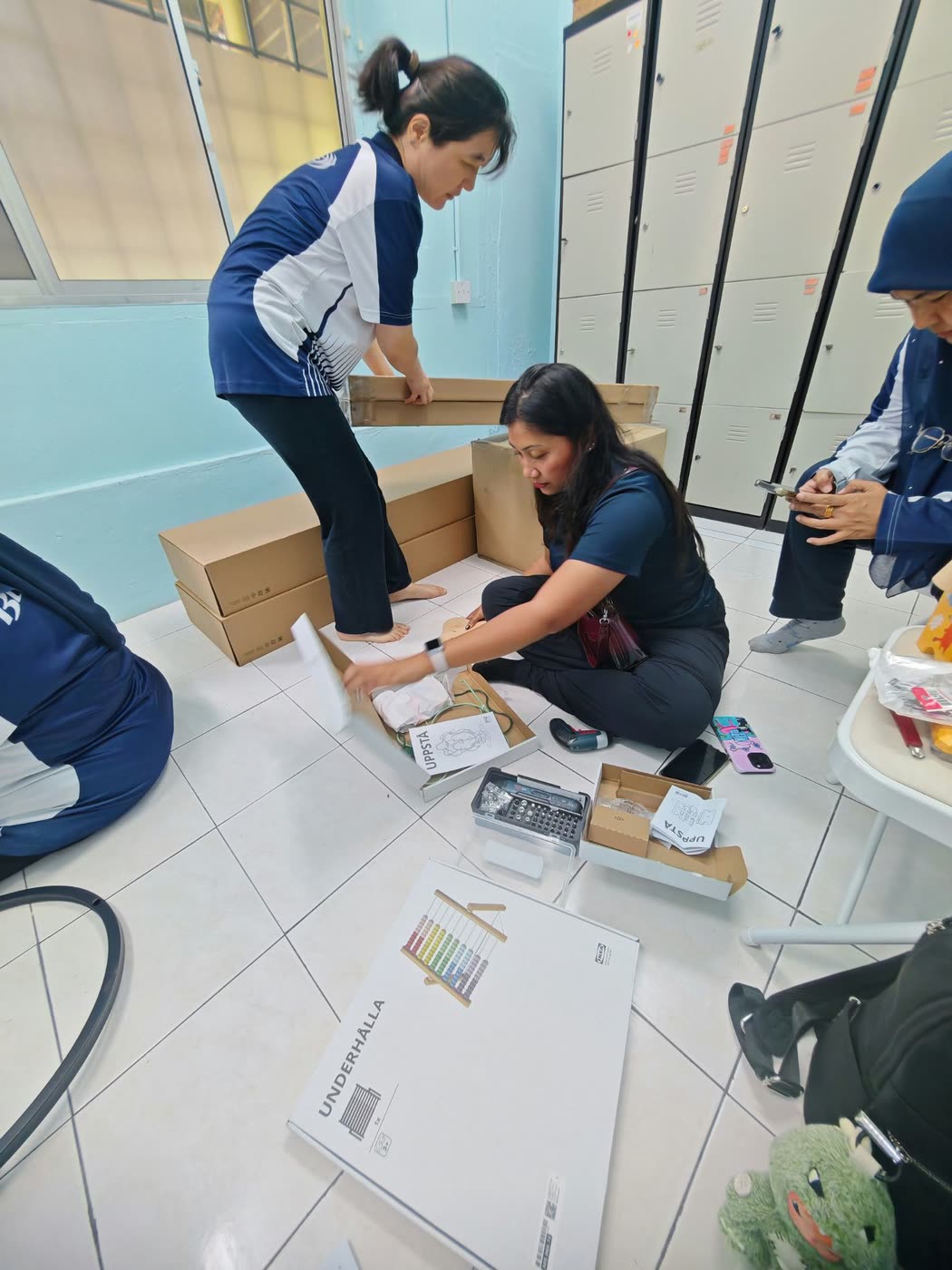 Committee members unboxing toys and furniture on the classroom floor